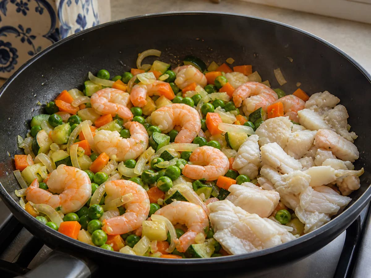 Preparação de Pescada e Camarões à Brás com Legumes durante a confeção